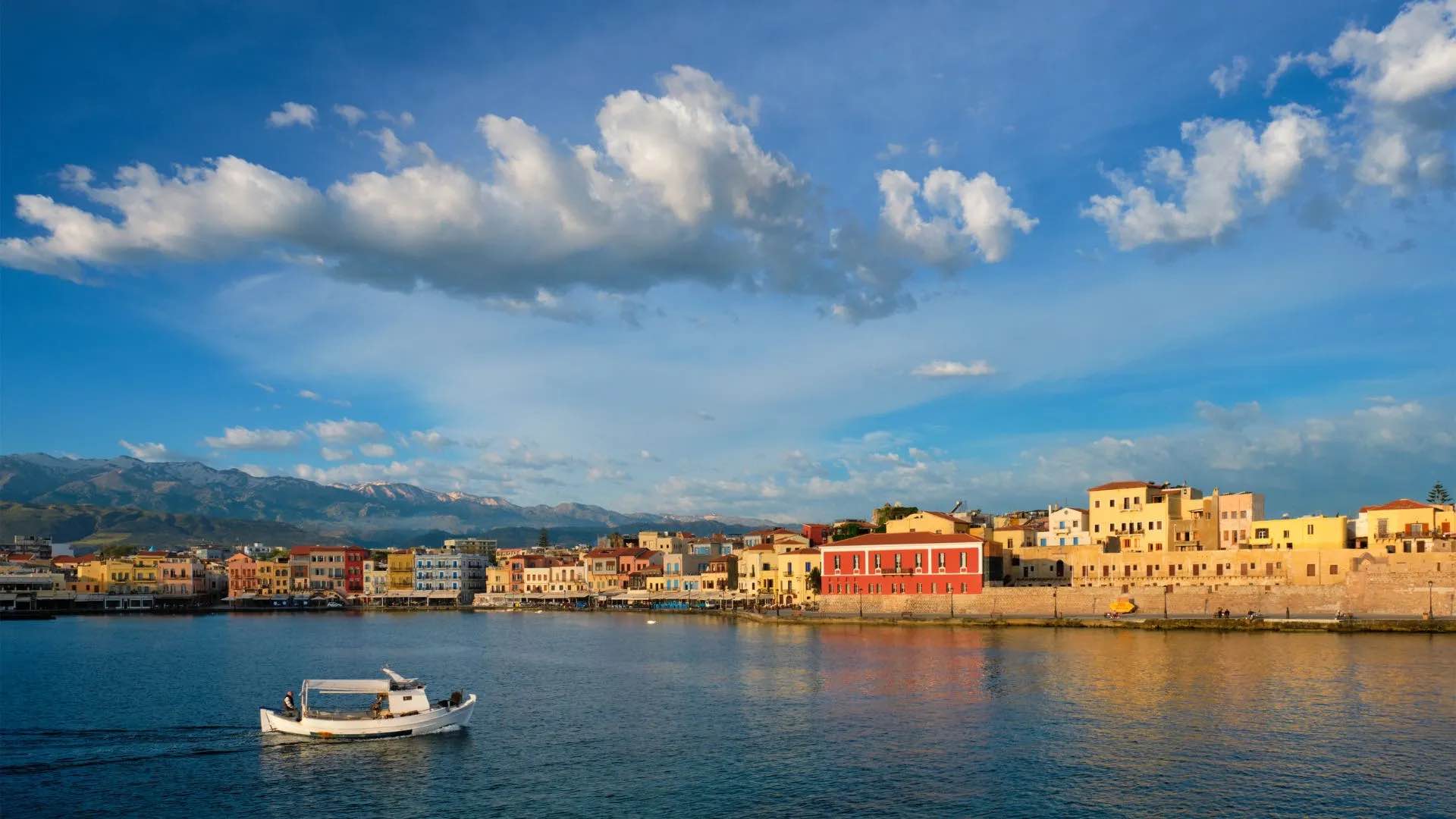 Bateau naviguant autour du port de Chania en Crète avec des maisons colorées et des montagnes en arrière-plan