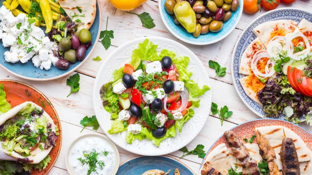 Table colorée avec des plats typiques de la cuisine crétoise : salade grecque, tzatziki, olives, pain pita et brochettes de viande.